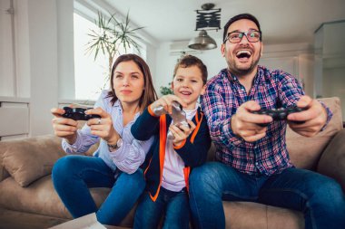 Mutlu aile kanepede oturuyor ve video oyunları oynamak ve yediğine