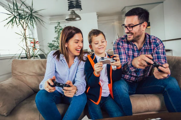 ソファーに坐っている幸せな家族とビデオゲームとイーティン — ストック写真