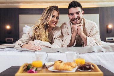 Lüks otel odasında kahvaltı eden genç mutlu çift. 