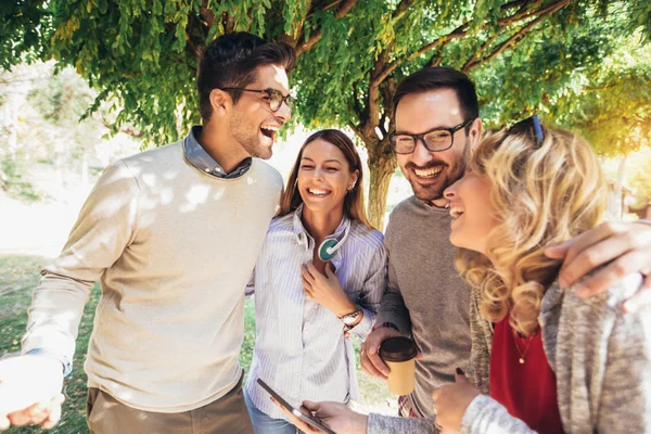 Vier fröhlich lächelnde junge Freunde, die draußen im Park spazieren gehen — Stockfoto