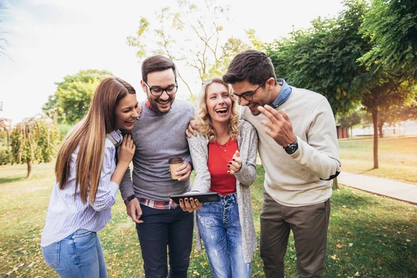 Vier fröhlich lächelnde junge Freunde, die draußen im Park spazieren gehen — Stockfoto