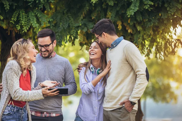 Vier fröhlich lächelnde junge Freunde, die draußen im Park spazieren gehen — Stockfoto