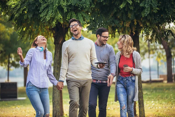 Vier fröhlich lächelnde junge Freunde, die draußen im Park spazieren gehen — Stockfoto