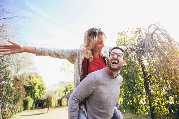 Couple having fun outdoor. Man giving piggyback to woman in park — Stock Photo, Image