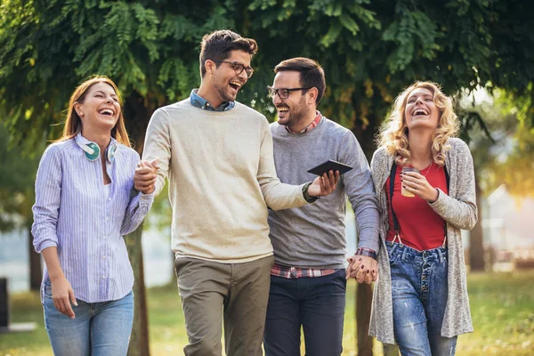 Cuatro felices jóvenes amigos sonrientes caminando al aire libre en el parque ho — Foto de Stock