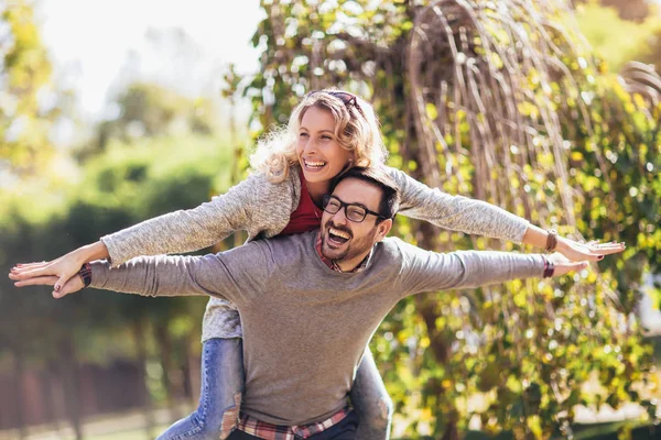 Par har roligt utomhus. Man ger piggyback till kvinna i park — Stockfoto