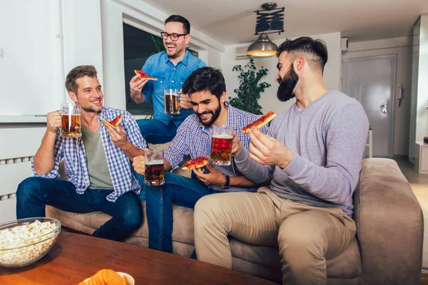 Группа из четырех друзей-мужчин пьет пиво и ест пиццу в доме — стоковое фото