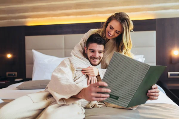 Coppia in camera d'albergo servizio in camera di lettura menu insieme a letto — Foto Stock