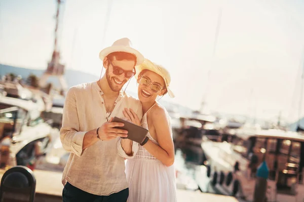 Heureux jeune couple marchant près du port en utilisant une tablette numérique de — Photo