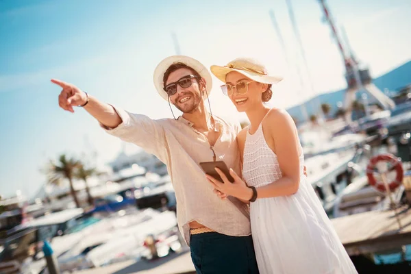Heureux jeune couple marchant près du port en utilisant une tablette numérique de — Photo