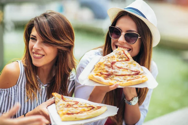Tre smukke unge kvinder, der spiser pizza efter shopping, har - Stock-foto
