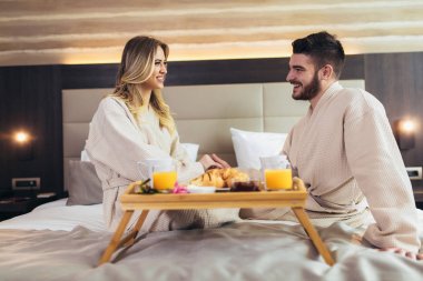 Lüks otel odasında kahvaltı eden genç mutlu çift. 