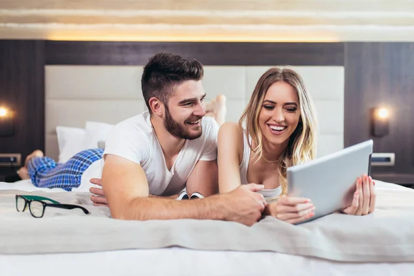 Happy young couple lying on the bed in a bedroom and using digit — Stock Photo, Image