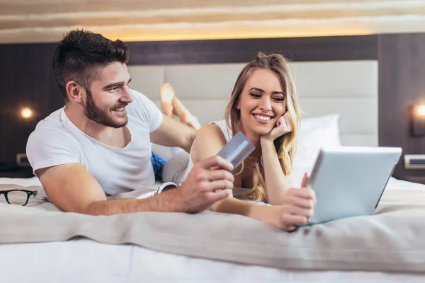 Pretty couple with credit card and digital tablet lying in bed a — Stock Photo, Image