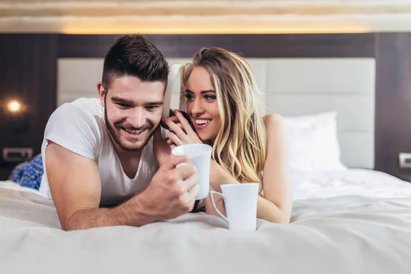 Sonriendo joven pareja en la cama bebiendo café y escuchando mus — Foto de Stock