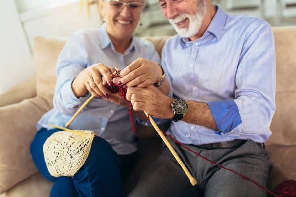 Senior woman teaching her husband the art of knitting woollen cl
