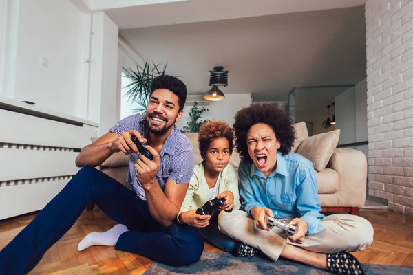 Familia sonriente sentada en el sofá jugando videojuegos — Foto de Stock