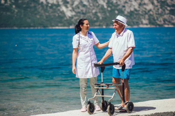 Enfermera ayudando a anciano mayor. Hombre mayor usando un andador con —  Fotos de Stock