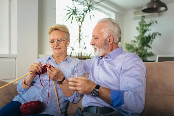 Senior woman teaching her husband the art of knitting woollen cl