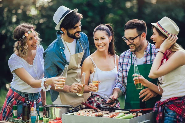 Młodzi przyjaciele bawiąc grillowanie mięsa korzystających grilla party. — Zdjęcie stockowe