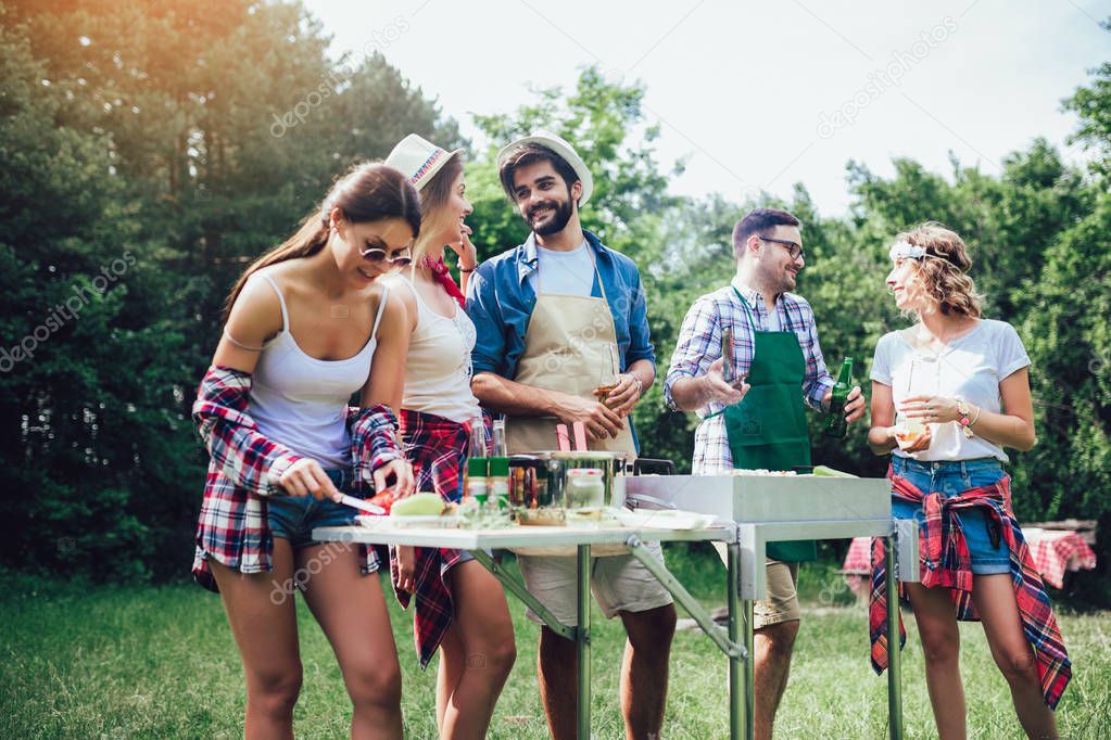 Young friends having fun grilling meat enjoying barbecue party.