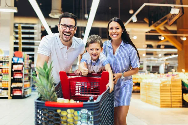 Lykkelig familie med barne- og handlevogn som kjøper mat på dagligvarer – stockfoto