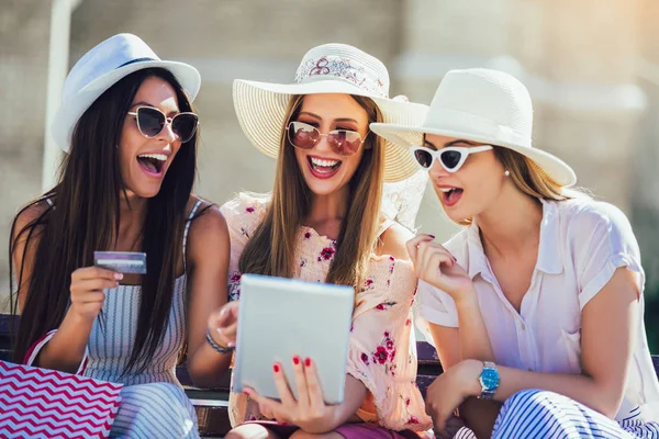 Trois filles avec des sacs à provisions colorés en utilisant une tablette numérique et — Photo