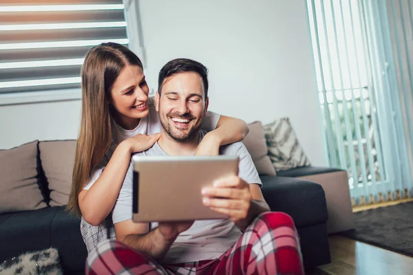 Pareja alegre usando una tableta en línea sentada en la sala de estar — Foto de Stock