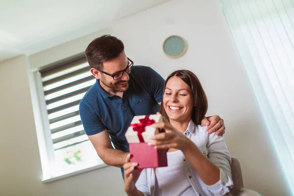 Uśmiechnięty mężczyzna zaskakuje swoją dziewczynę prezentem w domu — Zdjęcie stockowe