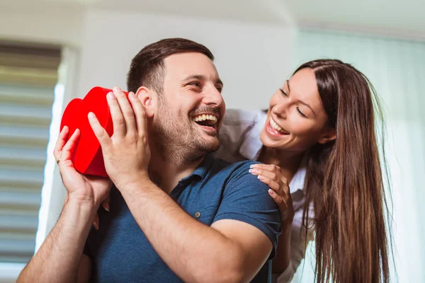 Uśmiechnięta kobieta zaskakuje swojego chłopaka z teraźniejszości w domu — Zdjęcie stockowe
