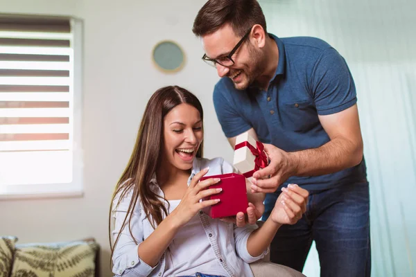 Улыбающийся мужчина удивляет свою девушку подарком дома — стоковое фото