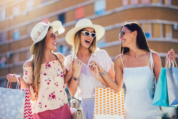Drie mooie meisjes in zonnebrillen met boodschappentassen in de stad. — Stockfoto