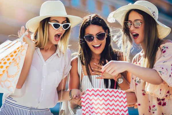 Drie mooie meisjes in zonnebrillen met boodschappentassen in de stad. — Stockfoto