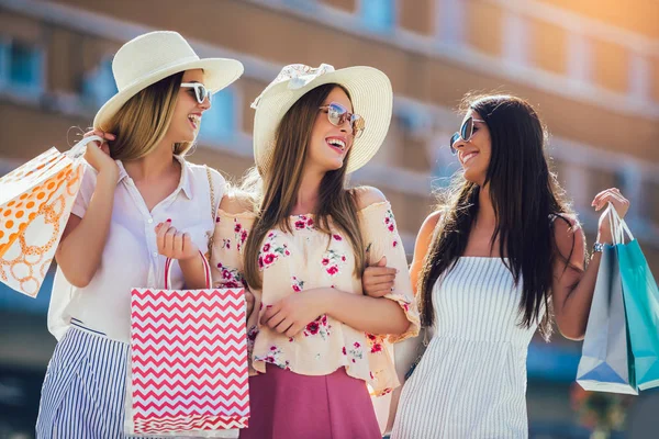Drie mooie meisjes in zonnebrillen met boodschappentassen in de stad. — Stockfoto