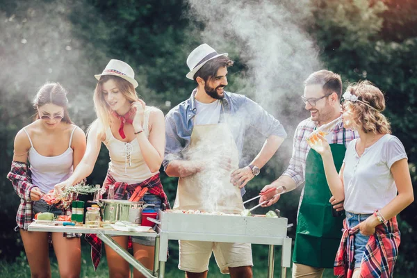 Jovens amigos se divertindo grelhando carne desfrutando de churrasqueira . — Fotografia de Stock