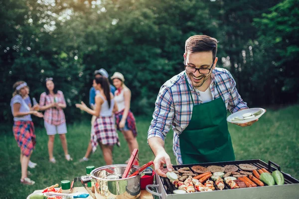 Bonito macho preparando churrasco ao ar livre para amigos — Fotografia de Stock
