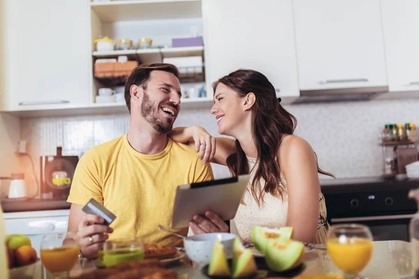 Улыбающаяся пара с помощью цифрового планшета и кредитной карты дома — стоковое фото