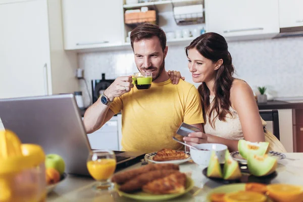 Улыбающаяся пара с помощью ноутбука и кредитной карты дома — стоковое фото