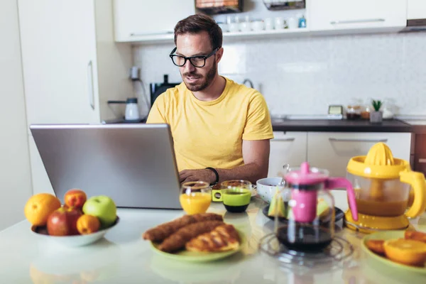 Занимательный мужчина, работающий дома, используя ноутбук во время завтрака . — стоковое фото