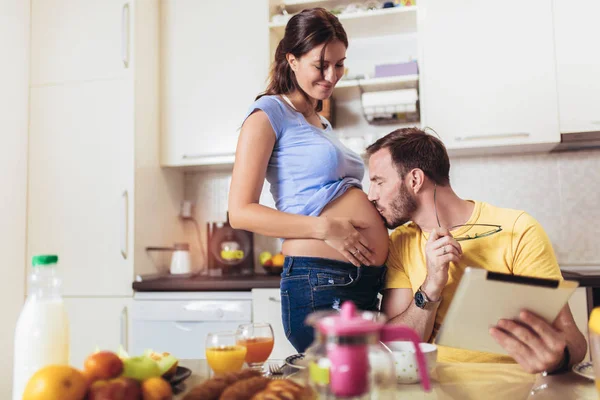 Pregnant woman with husband in the kitchen using digital tablet. — Stock Photo, Image