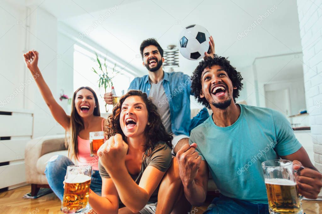 Happy friends or football fans watching soccer on tv and celebra