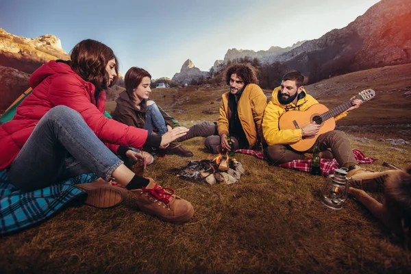 Grupo de amigos sonrientes sentados alrededor de la hoguera en el camping —  Fotos de Stock