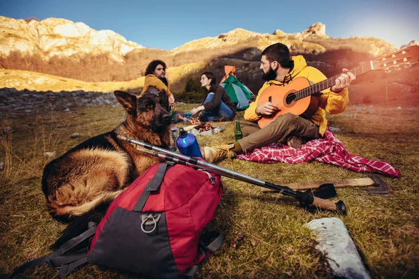 Gruppe af smilende venner sidder omkring bål på camping - Stock-foto