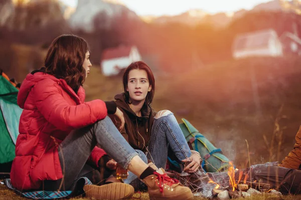 En gruppe smilende venner som sitter rundt bålet i telttur – stockfoto