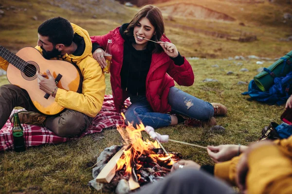 En gruppe smilende venner med marshmallow sittende rundt bålet – stockfoto