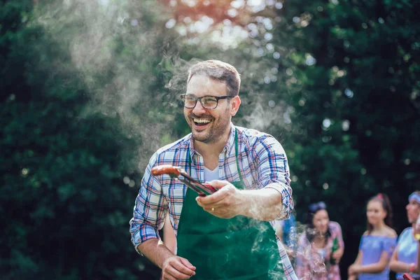 Красивый мужчина готовит барбекю на открытом воздухе для друзей — стоковое фото
