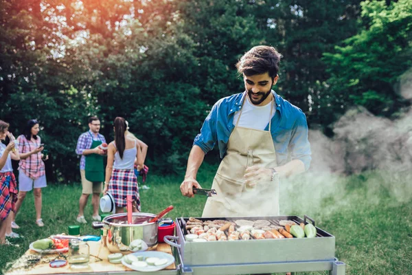Hombre guapo preparando barbacoa al aire libre para amigos — Foto de Stock