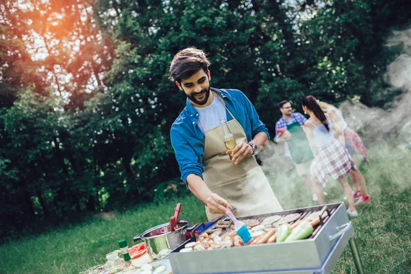 Kjekk mann som lager grillmat utendørs til venner – stockfoto
