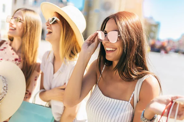 Tres hermosas chicas en gafas de sol con bolsas de compras en la ciudad . — Foto de Stock