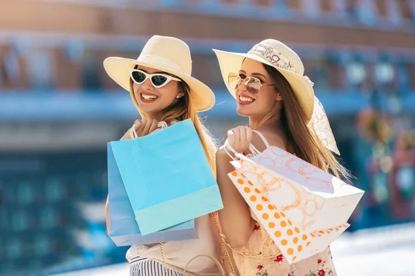 Two beautiful girls in sunglasses with shopping bags in city.